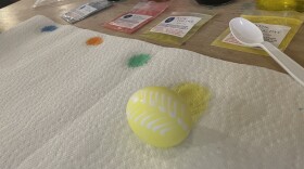 A recently dyed yellow egg rests on a paper towel in front of different colored dyes at an arts and crafts space in Charlottesville. 