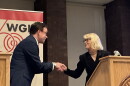A man and a woman shake hands at a podium 