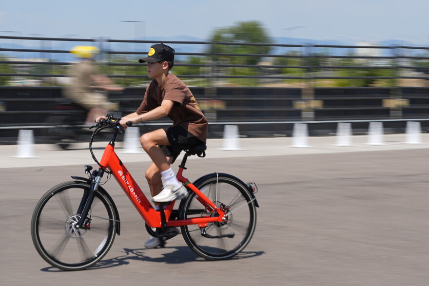 A boy in a baseball cap riding a bright red Bikabahn e-bike on a paved path.