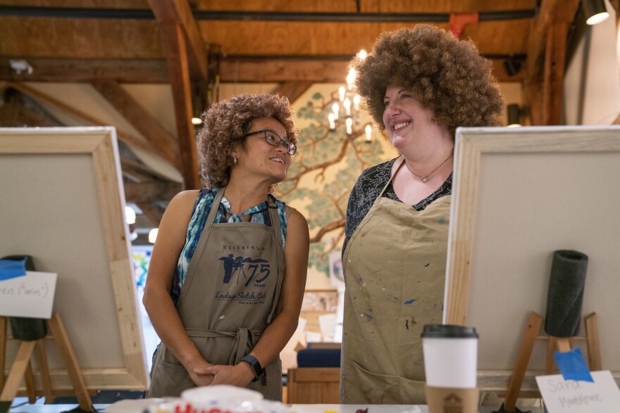 From left, Huyen MacMichael and Sara Monteleone exchange laughs during the Bob Ross painting class at the Franklin Park Arts Center. MacMichael and Monteleone wore the iconic Bob Ross wig during the entire class.