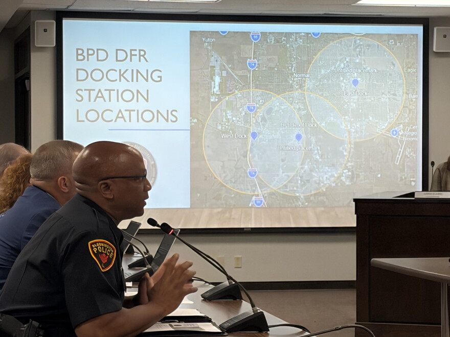 a police chief sits in the foreground, in the background a map shows locations for drone deployment docs in Bloomington