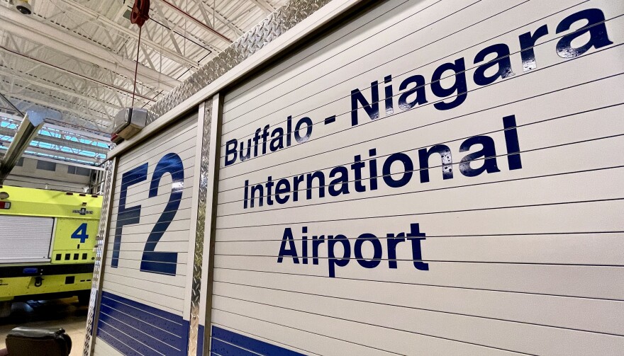  A Buffalo-Niagara International Airport emergency vehicle with white metal siding and blue lettering is pictured in a large storage hangar with a white ceiling. 