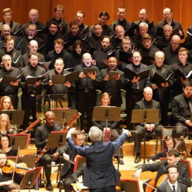 A man in a blue blazer conducts an orchestra