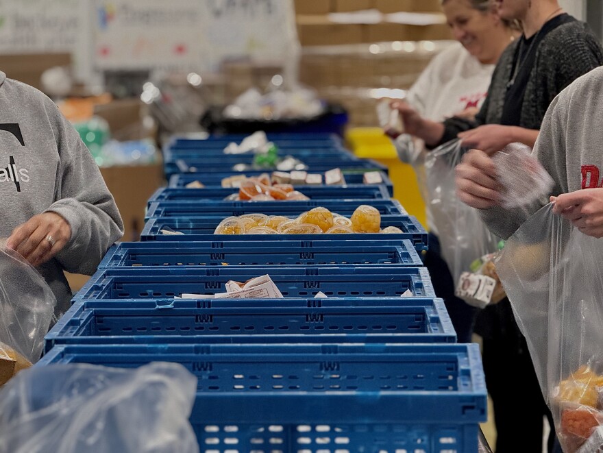 Staff at The Foodbank Inc. stand on either side of blue crates, filled with non-perishable items, to pack boxes 