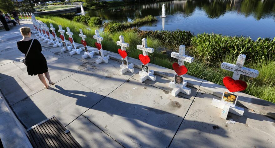 On the one-month anniversary of the Pulse nightclub massacre in Orlando, Fla., the mother of victim Amanda Alvear, Mayra Alvear, right, and Amanda's aunt, Robin Alvear, center, hand off the cross that was erected in Amanda's honor to Michael Perkins, left, of the Orange County Regional History Center, during a somber ceremony at Orlando Regional Medical Center, near the club, Tuesday, July 12, 2016. The 49 crosses were made by a Chicago carpenter to honor each of the victims killed at Pulse on June 12. The crosses will be on permanent display at the history center in downtown Orlando. (Joe Burbank/Orlando Sentinel via AP)