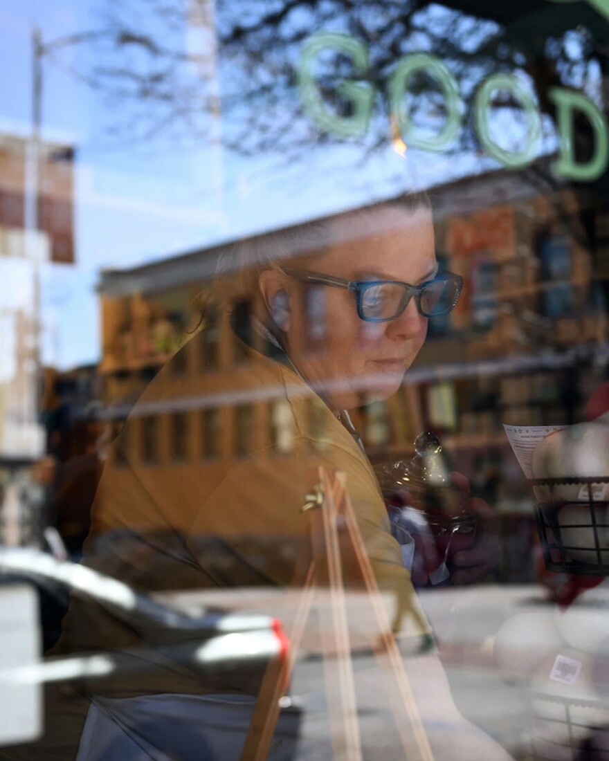 Leigh Lockhart is photographed through a window, placing items in her store.
