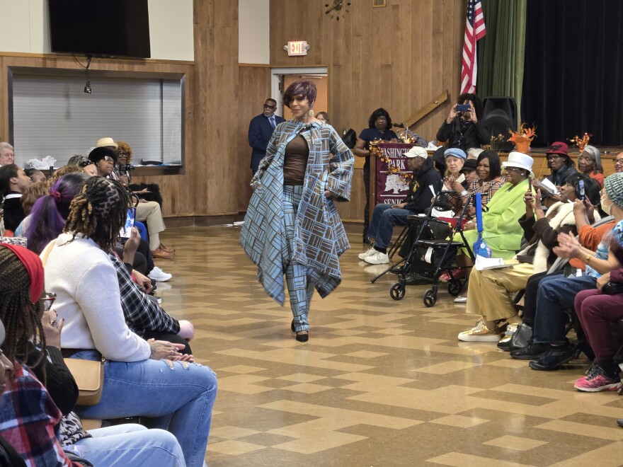Woman walking the runway in a chic bob haircut and a fashionable periwinkle blue and brown suit.