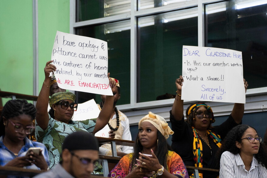 FILE - People hold signs during a speech by Charles Gladstone, a descendant of former plantation owner John Gladstone, as he delivers an apology on behalf of the Gladstone family at Georgetown University in Georgetown, Guyana, Friday, Aug. 25, 2023.