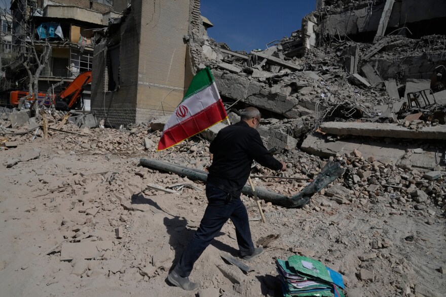 A man carries an Iranian flag to place on the rubble of a police facility struck during the U.S.–Israeli military campaign in Tehran, Iran, Wednesday, March 4, 2026. (AP Photo/Vahid Salemi)