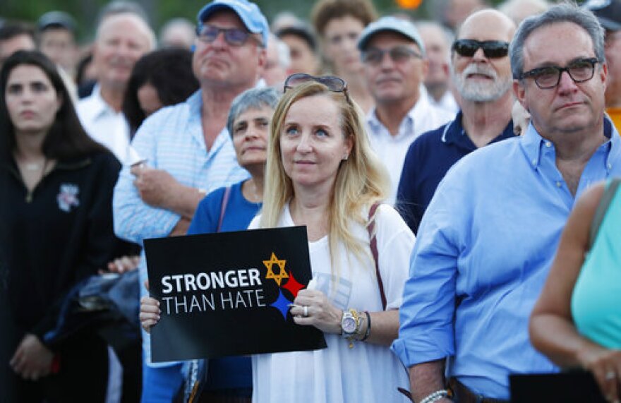 Iris Schaen, center, holds a sign as she listens to speakers during an interfaith vigil against anti-semitism and hate at the Holocaust Memorial, Tuesday, Oct. 30, 2018, in Miami Beach, Fla. 