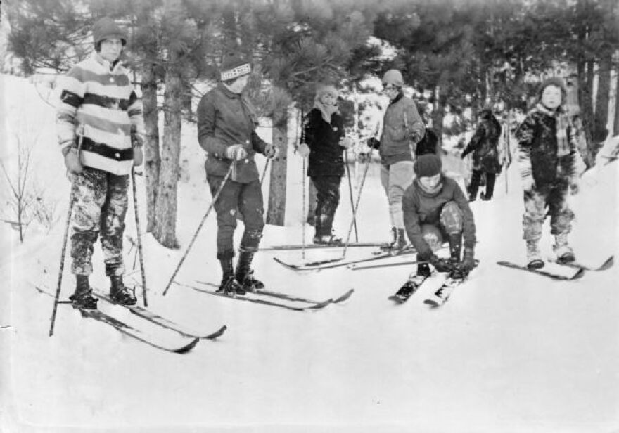 A group of skiers pose in front of pine trees around 1935.