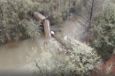 A collapsed railroad trestle with train cars in a river.