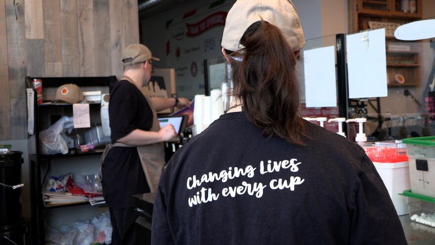 Kemeja karyawan memiliki bahasa yang mendorong dan inklusif, seperti 'Mengubah hidup dengan setiap cangkir.'