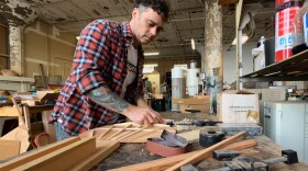 Man shaving wood frame of guitar in workshop.