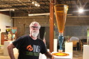 A man in a black t-shirt poses with a giant art sculpture made of glass