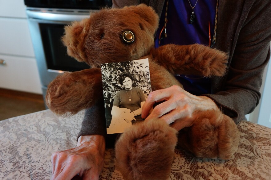 Woman holding a teddy bear in her arms and on the teddy bear holding a picture of her grandmother