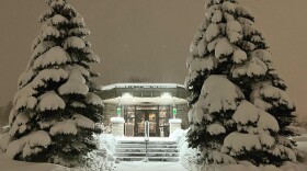 The KAXE studio against a dark sky flanked by snow covered balsam trees. 