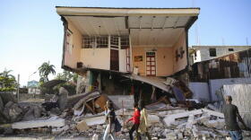 People walk past a home destroyed by the earthquake in Les Cayes, Haiti, Saturday, Aug. 14, 2021. A 7.2 magnitude earthquake struck Haiti on Saturday, with the epicenter about 125 kilometers (78 miles) west of the capital of Port- au-Prince, the US Geological Survey said. 