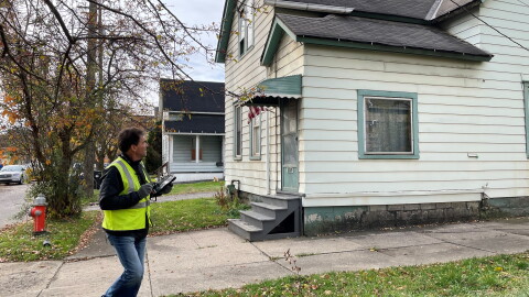 A man in a bright yellow safety vest inspects the exterior of a house in Cleveland. 