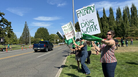 People hold signs and protest along the side of a road. 