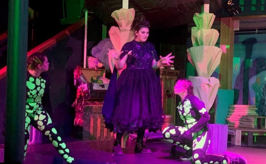 Three kids on stage where two are wearing neon green spotted suits and the other in witch like clothing.