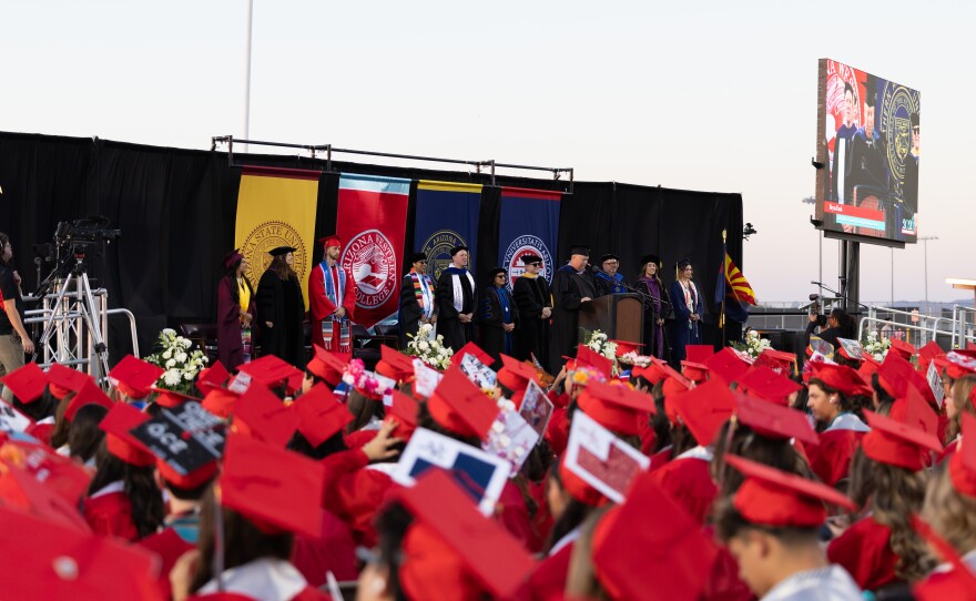 A sea of red graduation caps looks on at the leadership representing AWC, ASU, NAU and UA.