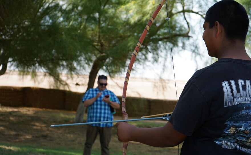 A student holds up a bow and arrow during an archery lesson.