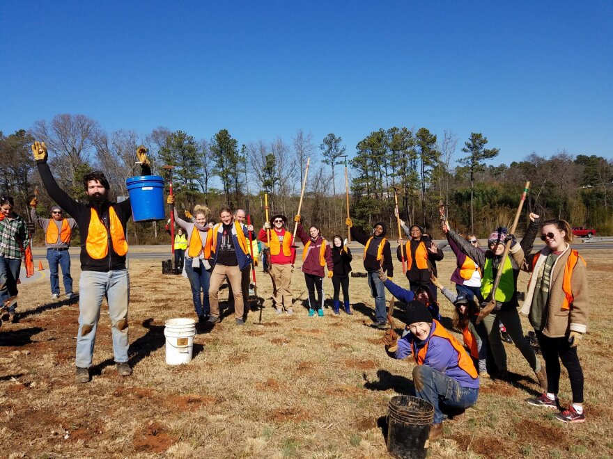 A crowd of volunteers wearing safety vests, hoisting their shovels and buckets up in the air in celebration outside at a site for the Martin Luther King Jr. Day of Service in 2023