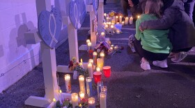 Vigil attendees kneel in front of five crosses, one for each person confirmed dead at the time of the vigil.