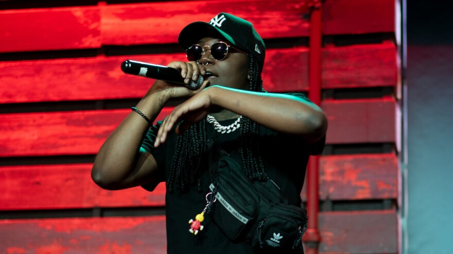  A woman wearing dark glasses and a New York Yankees cap raps into a microphone on stage in a small performance space.