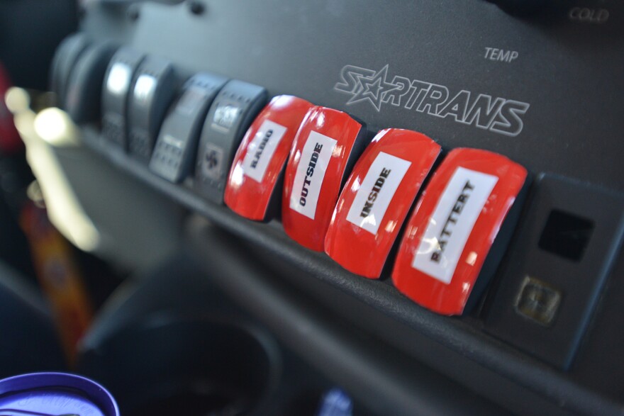 A row of red buttons on a black dashboard read from left to right: "Radio, Outside, Inside, Battery."