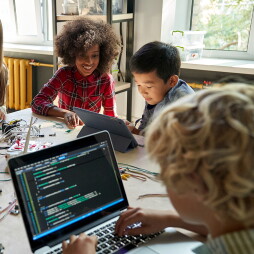 Diverse school children students build robotic cars using computers and coding. Happy multiethnic kids learning programming robot vehicles sitting at table at STEM education science engineering class.