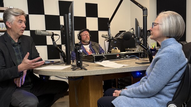 Three people sitting in a radio studio speaking into microphones
