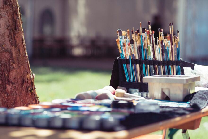 paints and paint brushes are set up near a tree in the sunshine.