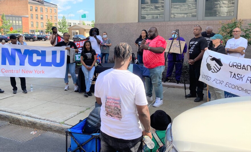 Ryedell Davis speaks to the crowd gathered between Syracuse City Hall and the state office building. The I-81/I-690 interchange can be seen in the distance.