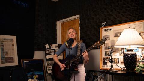 Evelyn Winn plays guitar in a corner filled with UPR memorabilia.