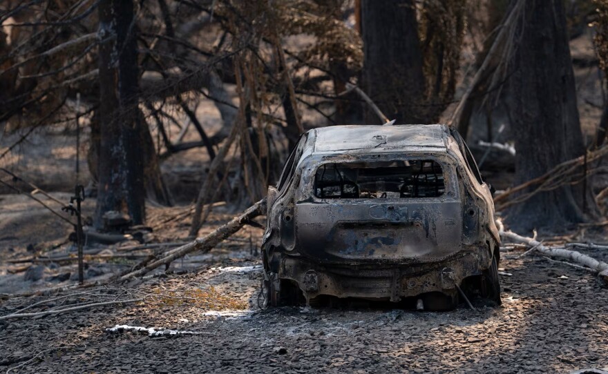 A burned car sits near a house that was destroyed by the fire.