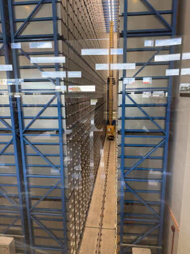 Tall blue steel racks of storage bins inside the Central Library's automated book retrieval system, seen through glass