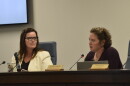 Two women sit at a desk with microphones. 