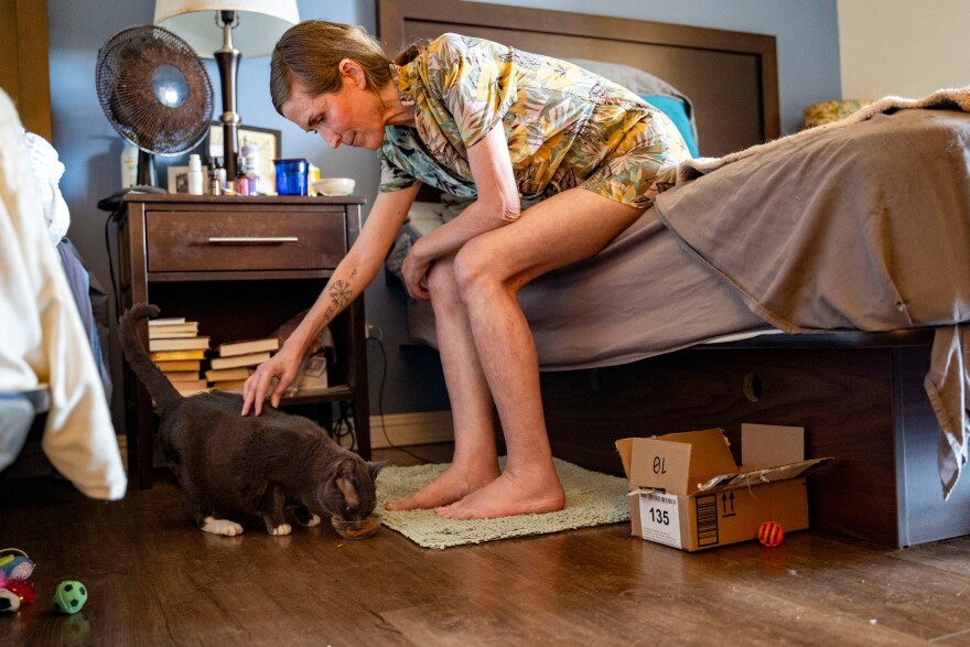 Mari Younger pets her cat Stella inside her converted hotel room where she lives after being displaced two years prior by the Maui fires, in Kīhei, Hawaiʻi, Wednesday, March 4, 2026.