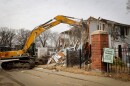 A construction truck begins tearing down a crumbling and graffiti-covered building.