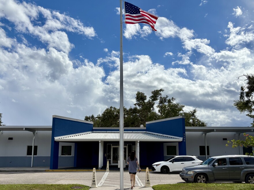 Blue school building with a tall US flagpole in the middle and a female walking toward the front door