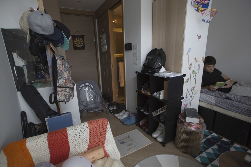 In this June 10, 2017 photo, Donny Chan reads on his bed at his apartment, one of a growing number of tiny, upscale units known as "microflats" in Hong Kong. Hong Kong’s property developers are scaling down, way down, for younger, middle-class buyers, offering micro-sized upscale apartments with stratospheric price tags. (AP Photo/Kin Cheung)