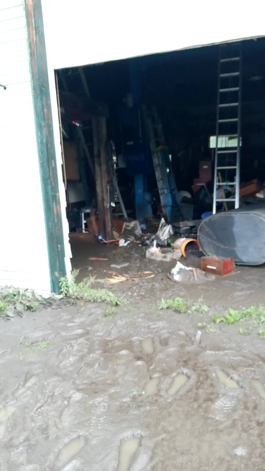 Wet mud in a garage with garbage and a propane tank on its side