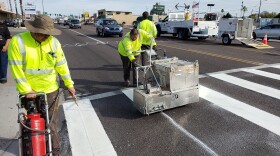 Workers upgrade a standard parallel line crosswalk to a high-visibility crosswalk at 19th and Fairmount avenues in Phoenix.