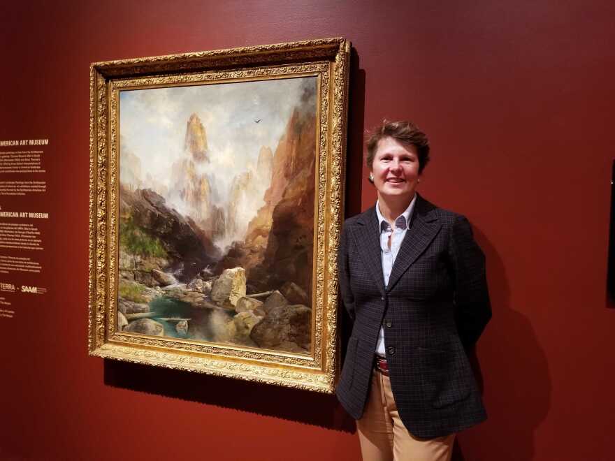 A woman standing in front of a large nineteenth century painting hanging in a museum.