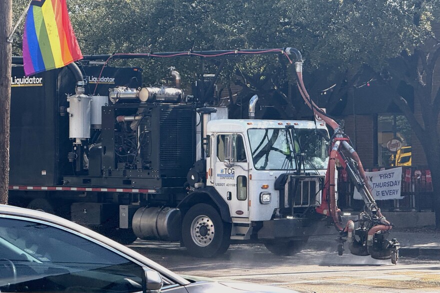A large truck labeled "Liquidator" affixed with a power washer sprays water on a street.