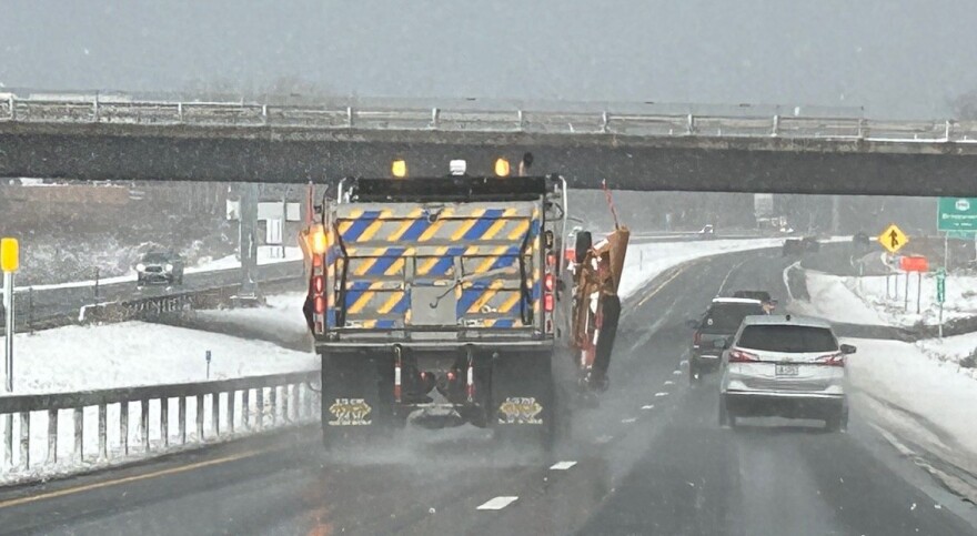 A snowplow and several cars on a highway near Syracuse with snow on the ground