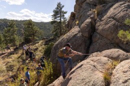 Hikers climb up a rock with a rope.