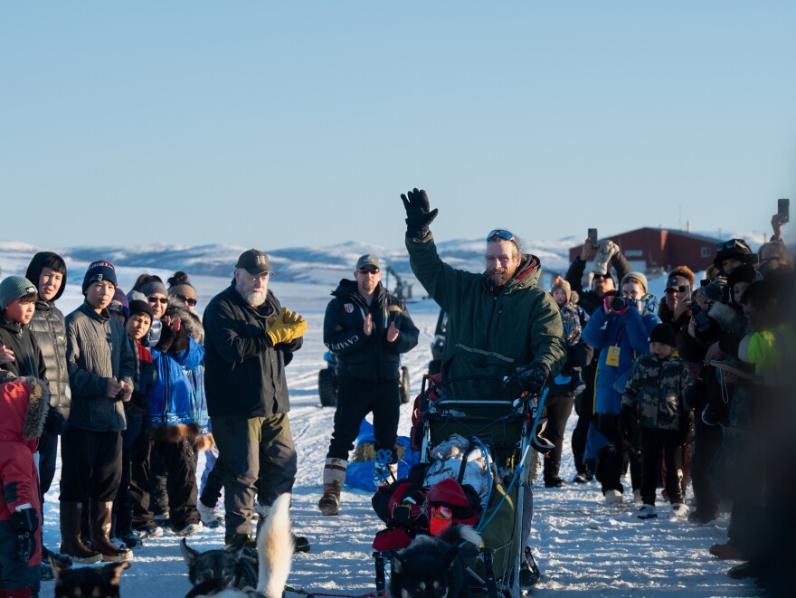An Iditarod musher waves to fans